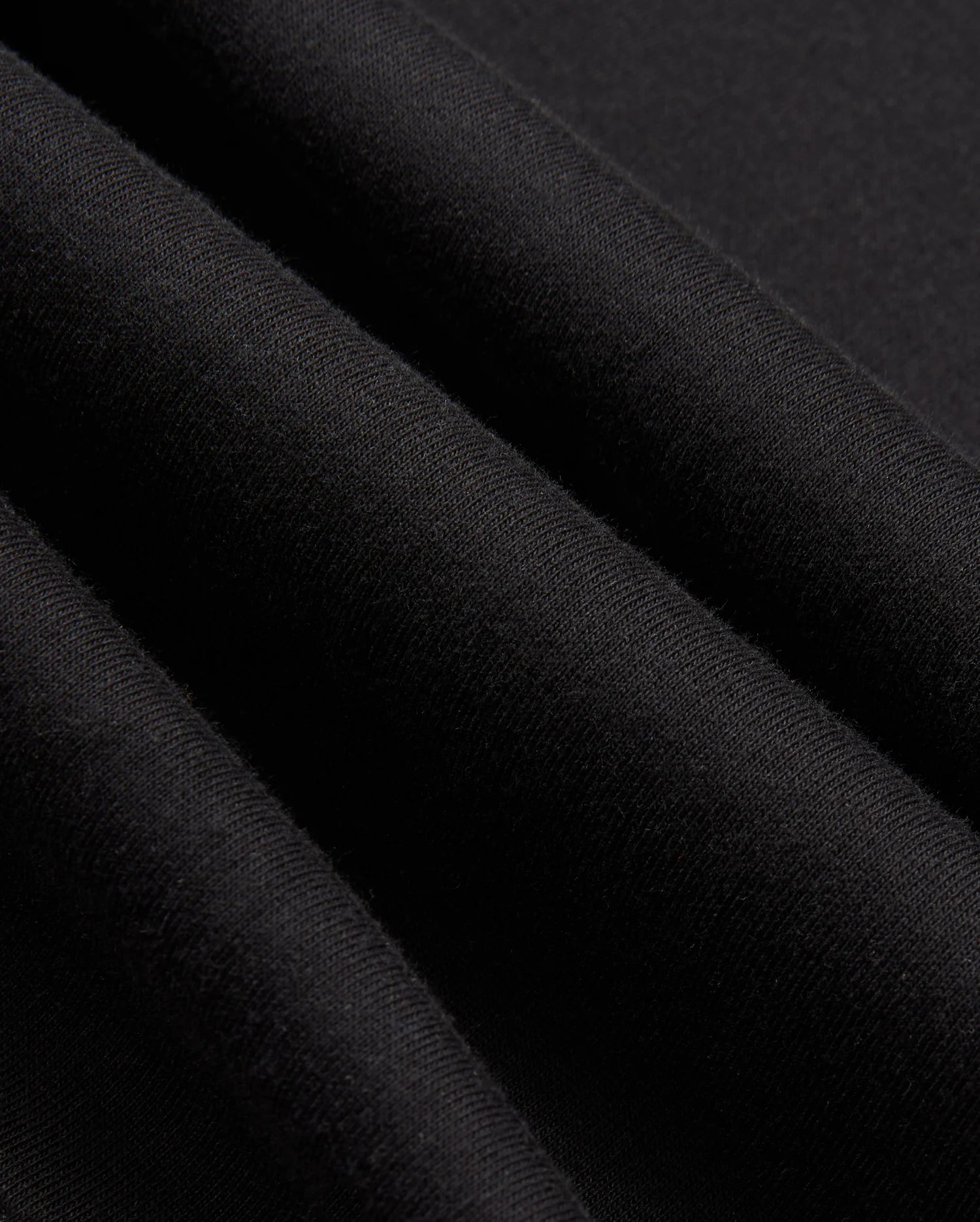 Close-up of black fabric revealing its woven texture and soft sheen, evocative of a high-quality jersey. The material appears smooth and slightly folded, suggesting the stylish warmth you'd expect from the Psycho Bunny Mens James Premium Zip Hoodie - B6H793D200.