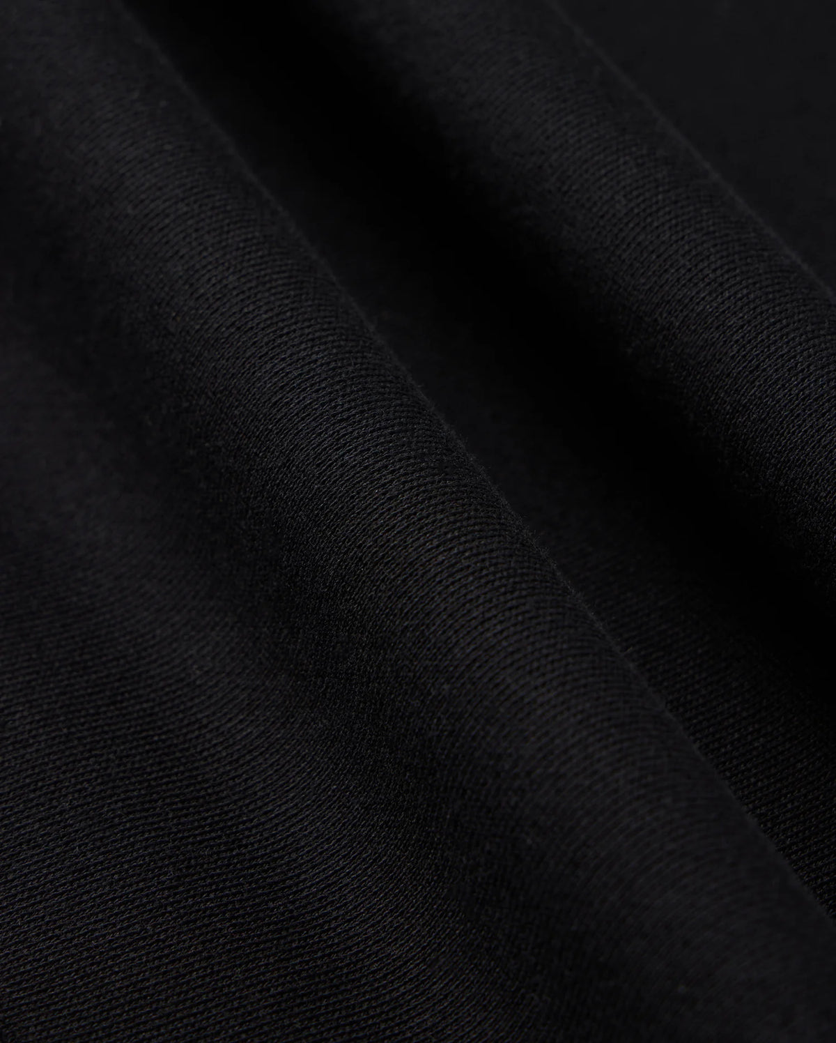 Close-up image of black fabric with a slight texture and soft folds. The surface appears smooth with fine, even weave, showcasing the material's quality and depth. Perfectly suited for a Psycho Bunny Men's Levy Fleece Hoodie (B6H859D200), crafted from 100% cotton for comfort and durability.