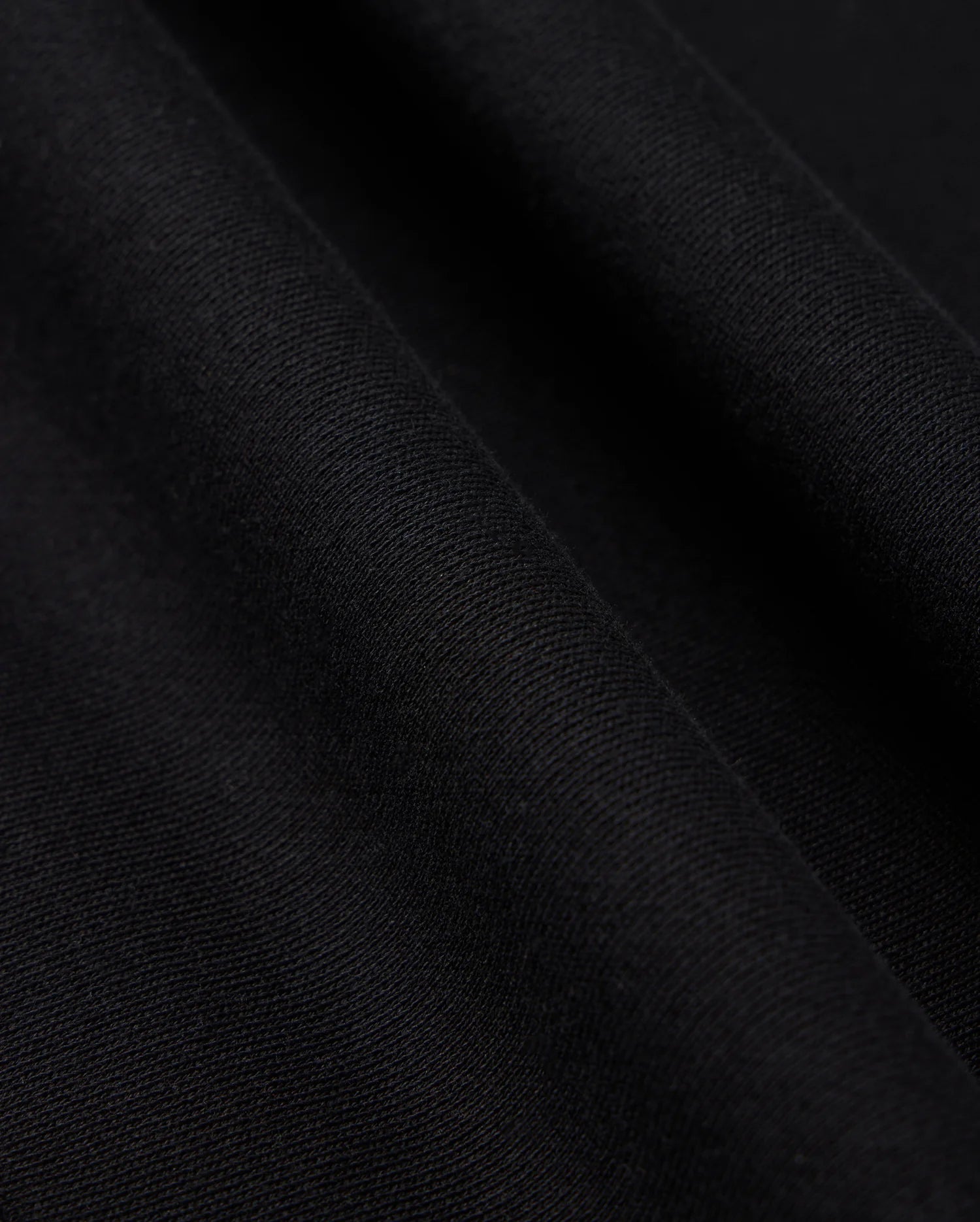 Close-up image of black fabric with a slight texture and soft folds. The surface appears smooth with fine, even weave, showcasing the material's quality and depth. Perfectly suited for a Psycho Bunny Men's Levy Fleece Hoodie (B6H859D200), crafted from 100% cotton for comfort and durability.