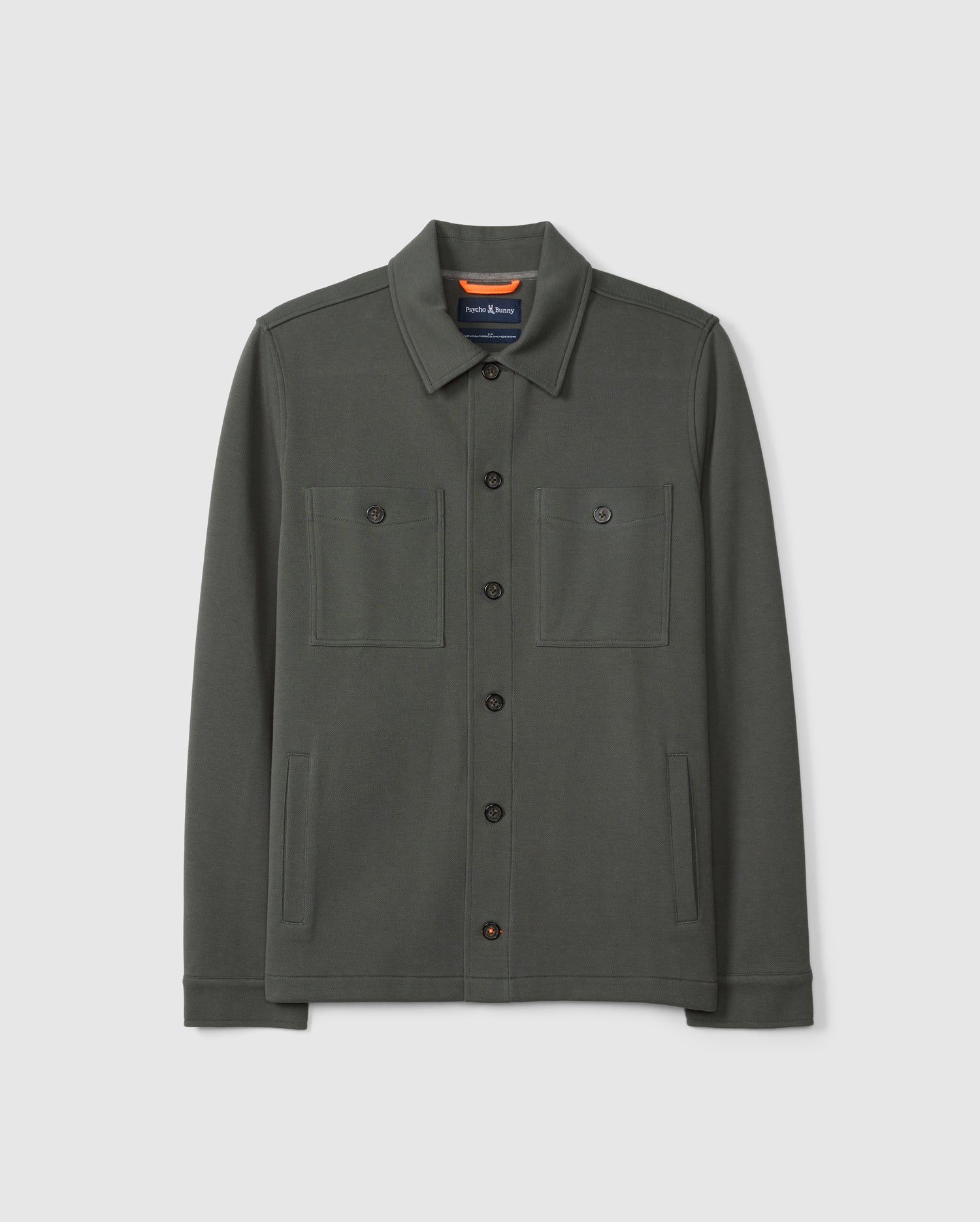 The MENS BEDFORD SHIRT JACKET B6J290B200 by Psycho Bunny is a dark green cotton-blend button-up with a collar and two chest pockets, adding an urban feel to any outfit against a plain white background.