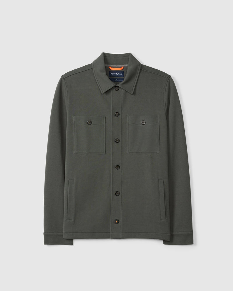 The MENS BEDFORD SHIRT JACKET B6J290B200 by Psycho Bunny is a dark green cotton-blend button-up with a collar and two chest pockets, adding an urban feel to any outfit against a plain white background.