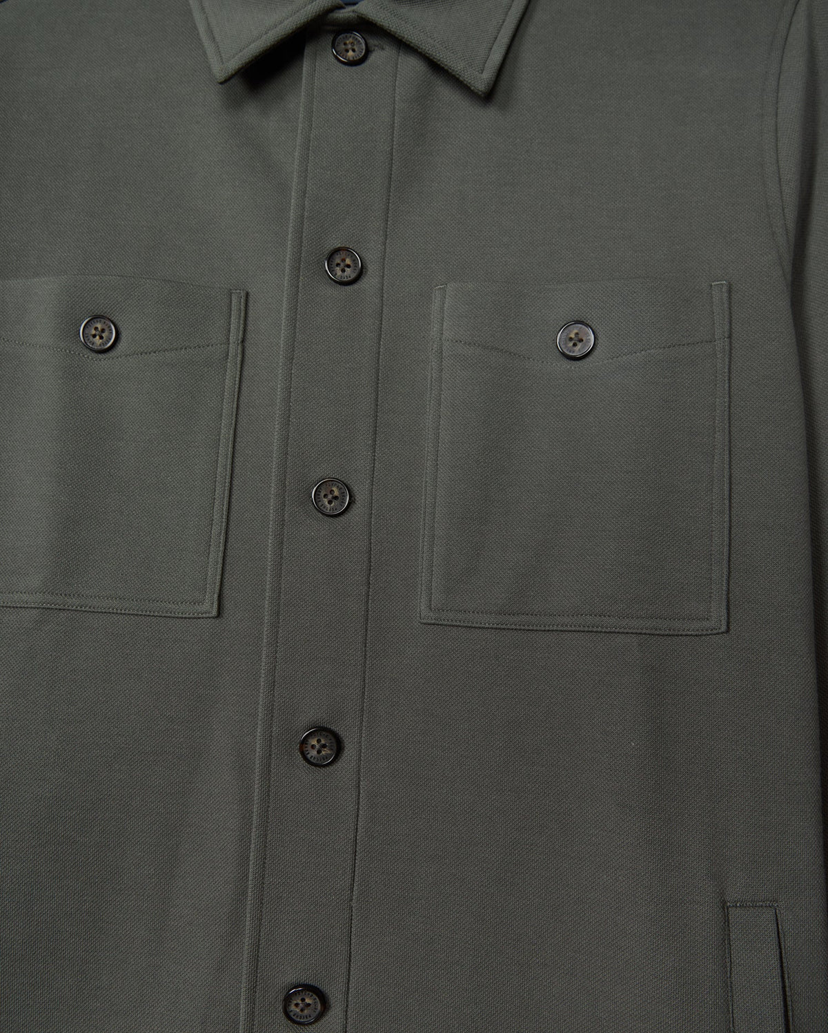 Close-up of the Psycho Bunny Men's Bedford Shirt Jacket (B6J290B200) in dark green cotton-blend. The urban-style jacket highlights two chest pockets, black buttons, neatly stitched seams, and a fold-over collar.