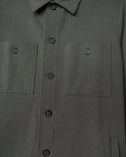 Close-up of the Psycho Bunny Men's Bedford Shirt Jacket (B6J290B200) in dark green cotton-blend. The urban-style jacket highlights two chest pockets, black buttons, neatly stitched seams, and a fold-over collar.