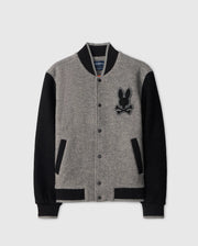 The MENS TOM WOOL BOMBER JACKET - B6J744D200 by Psycho Bunny is a stylish option with a grey body and black sleeves. It features black ribbed collar, cuffs, and hem, as well as a black embroidered patch on the left chest depicting a cartoonish rabbit's head with crossbones.