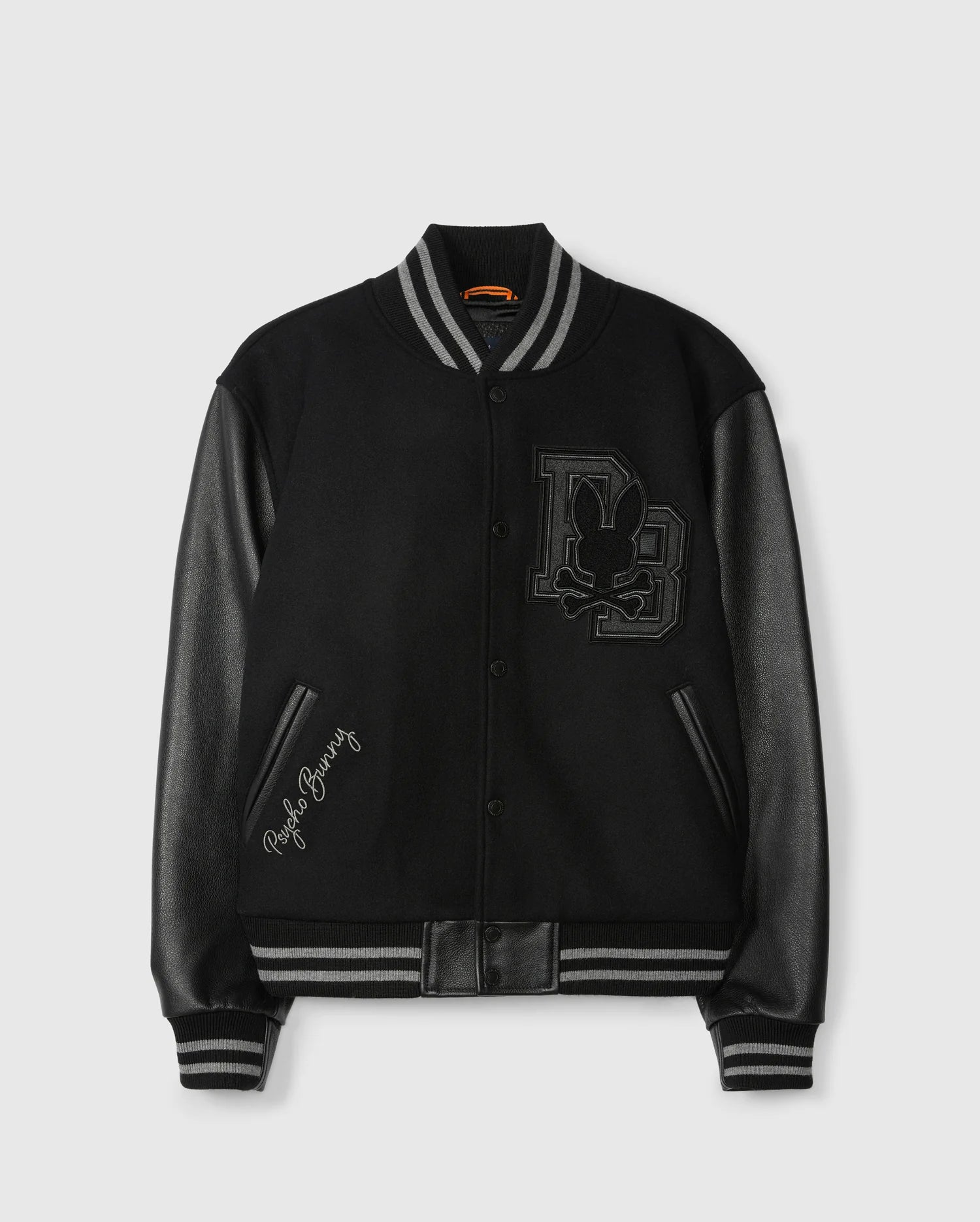 Introducing the Psycho Bunny Men's Brayden Wool Leather Varsity Bomber (B6J876D200), a stylish jacket crafted with a black wool blend and accentuated by leather sleeves. The design features ribbed cuffs and a collar, along with a prominent emblem displaying a stylized rabbit and the initials "DB" on the front. Additionally, one sleeve is elegantly embroidered with "Playboy Bunny.