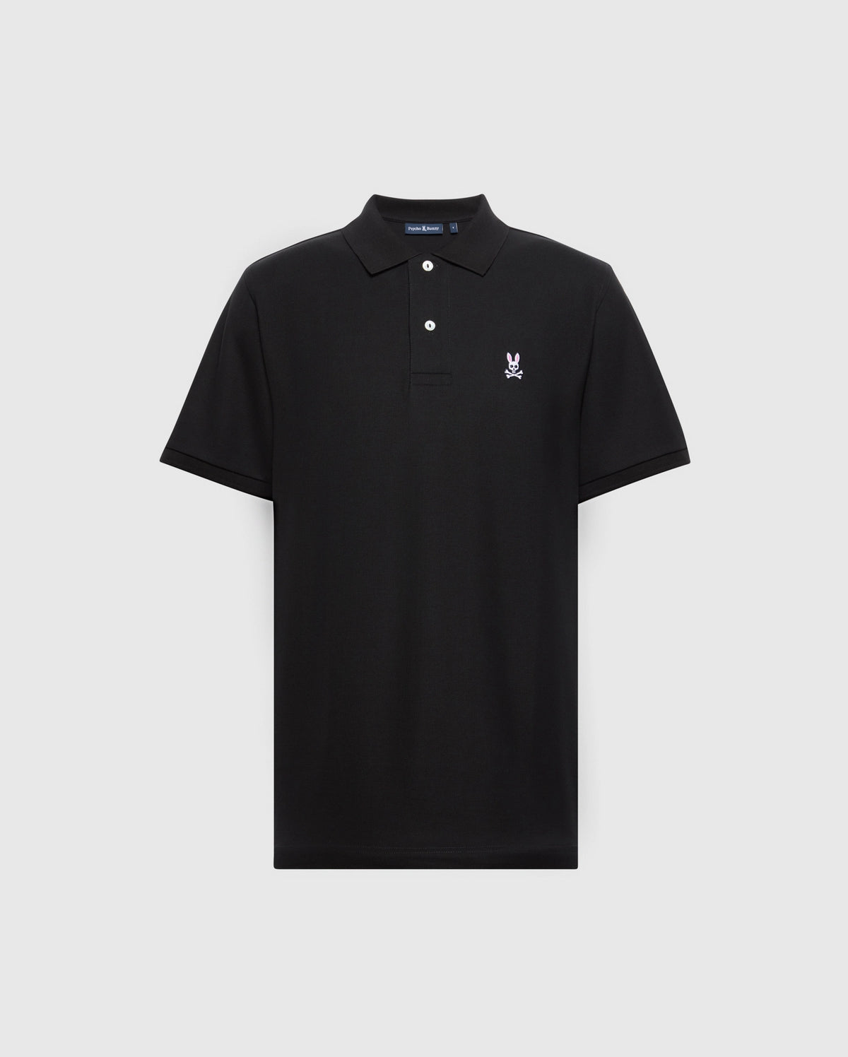 The Psycho Bunny Men's Classic Pique Polo Shirt (B6K001ARPC) is black, made from 100% Pima cotton, and features a small embroidered rabbit and crossbones logo on the left chest. It has a classic collar with a two-button placket adorned with sleek mother-of-pearl buttons against a light gray background.