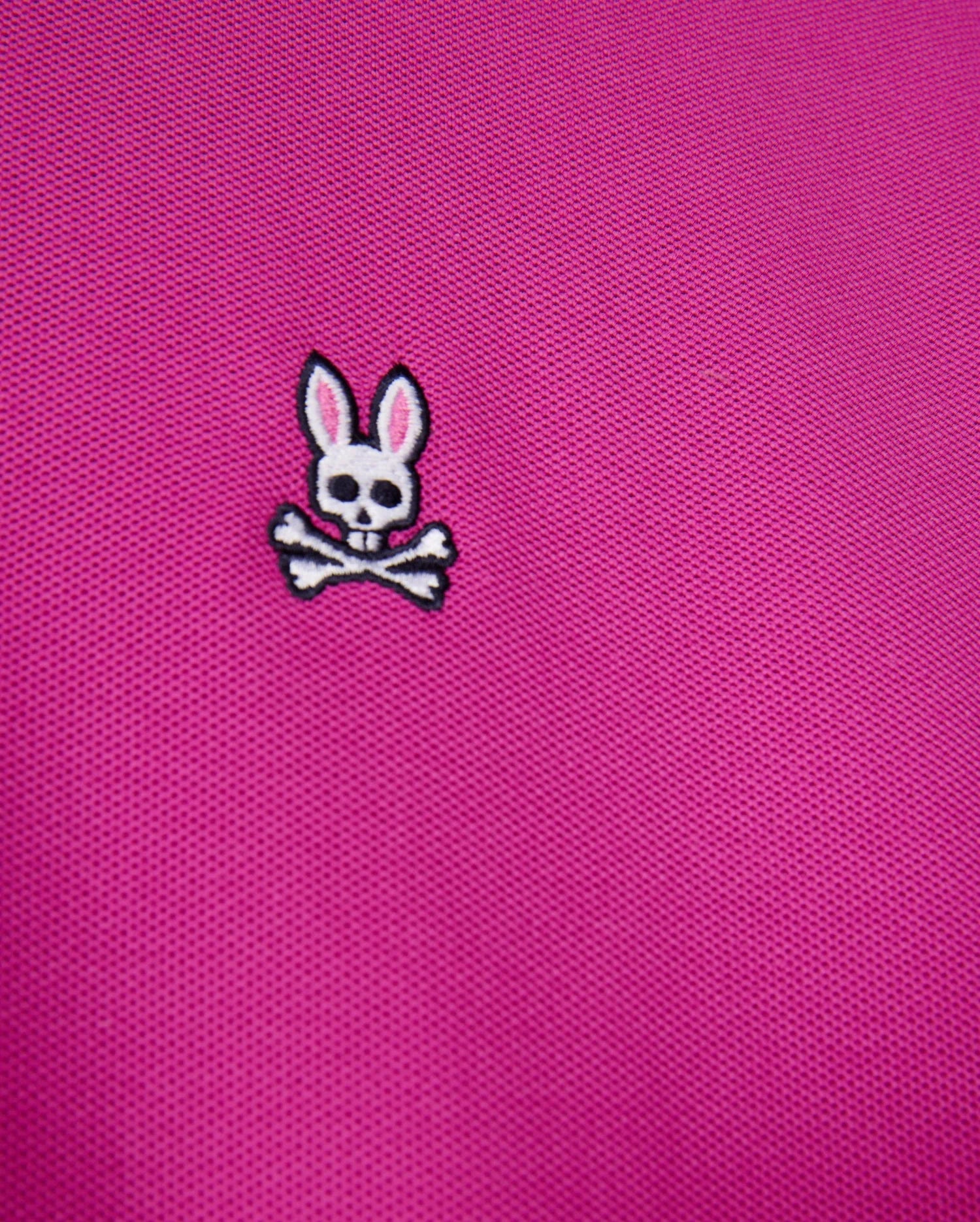 The Psycho Bunny MENS CLASSIC PIQUE POLO SHIRT - B6K001D200 features pink textured 100% Pima cotton with an embroidered white skull and crossbones topped with rabbit ears.