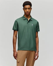 A man wears the Psycho Bunny MENS CLASSIC PIQUE POLO - B6K001F200, featuring an embroidered Bunny logo, with tan cargo pants against a light gray background.