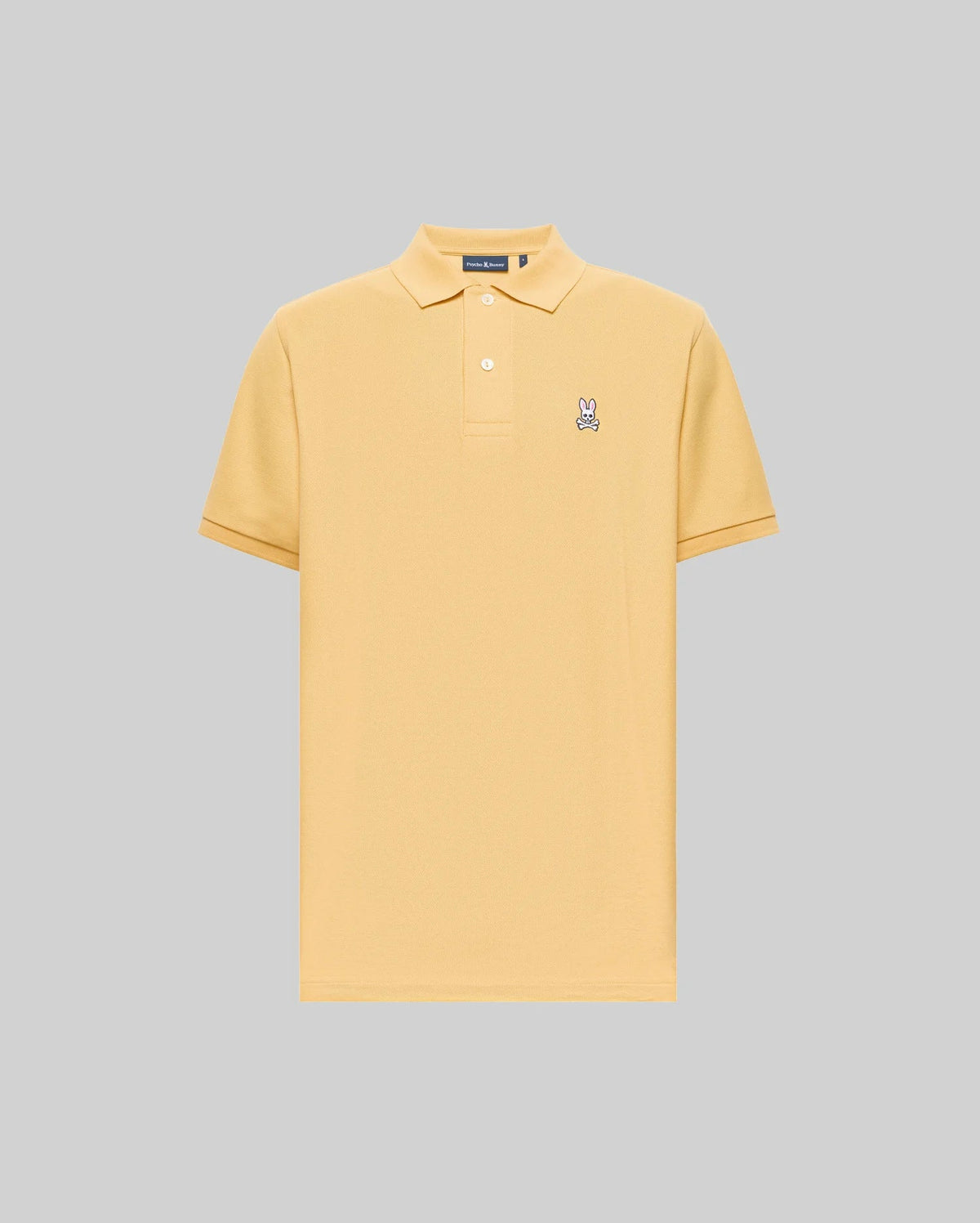 The Psycho Bunny MENS CLASSIC PIQUE POLO - B6K001F200 is a light yellow, short-sleeve Pima cotton polo with a collar, two buttons, and an embroidered Bunny logo on the left chest, set against a plain gray background.