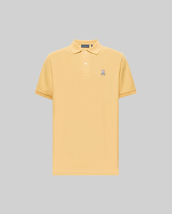 The Psycho Bunny MENS CLASSIC PIQUE POLO - B6K001F200 is a light yellow, short-sleeve Pima cotton polo with a collar, two buttons, and an embroidered Bunny logo on the left chest, set against a plain gray background.