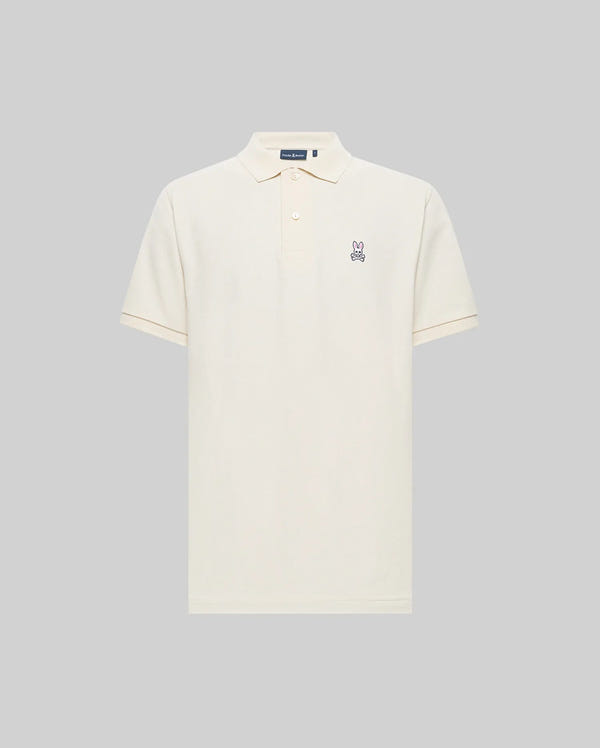 The Psycho Bunny MENS CLASSIC PIQUE POLO SHIRT (B6K001F200) in cream is made from soft Pima cotton, featuring short sleeves, a collar with three buttons, and an embroidered Bunny logo on the left chest. Shown against a light gray background.