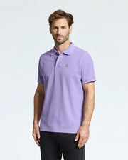 A man with short hair wears a Psycho Bunny's MENS CLASSIC PIQUE POLO SHIRT - B6K001Z1PC in light purple, featuring a subtle Bunny logo, paired with black pants against a plain white background.