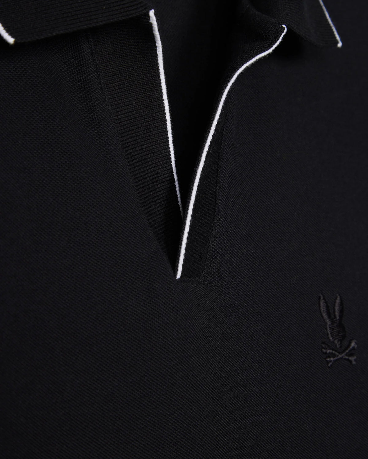 Close-up of a black Pima cotton MENS EAST HILLS JOHNNY COLLAR POLO SHIRT - B6K331B200 by Psycho Bunny with contrasting white piping along the Johnny collar. The shirt features an embroidered logo of a rabbit with crossbones on the left chest. The fabric texture is evident, giving it a premium, solid pattern look.