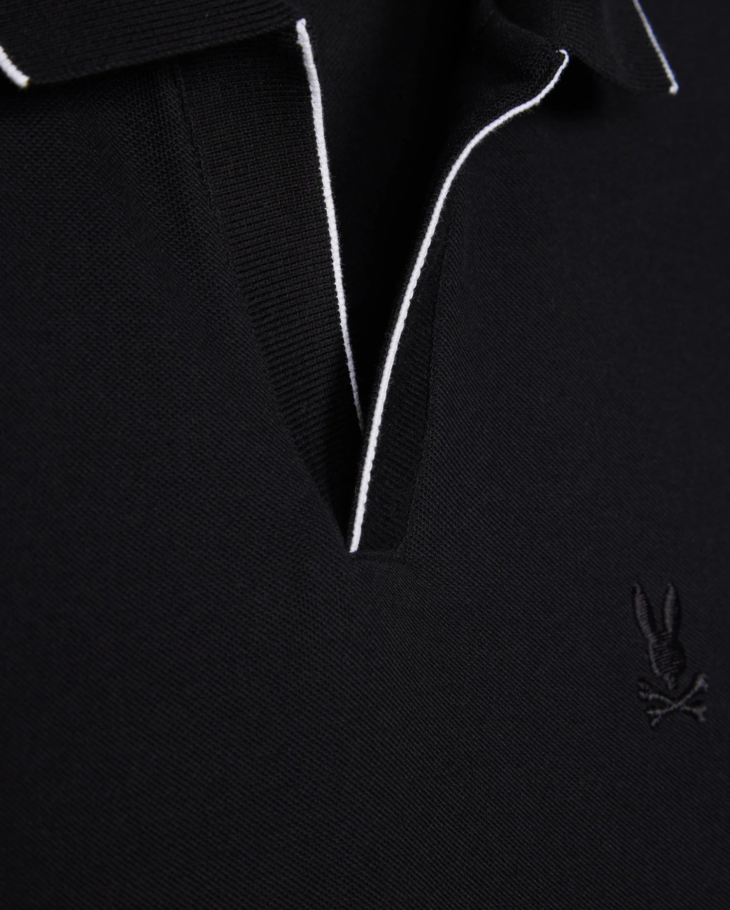 Close-up of a black Pima cotton MENS EAST HILLS JOHNNY COLLAR POLO SHIRT - B6K331B200 by Psycho Bunny with contrasting white piping along the Johnny collar. The shirt features an embroidered logo of a rabbit with crossbones on the left chest. The fabric texture is evident, giving it a premium, solid pattern look.