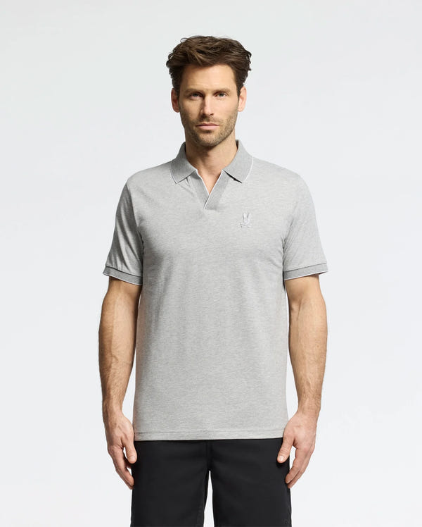 A man with short brown hair and a trimmed beard wears the Psycho Bunny MENS MACKAY JACQUARD JOHNNY COLLAR POLO (B6K408F200) in light gray and black pants, standing against a plain white background.