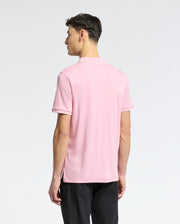 A man with short, dark hair faces away, wearing Psycho Bunny's Mens Bryce Performance Pique Polo - B6K486F200 in light pink made from breathable moisture-wicking fabric and black pants against a plain white background.