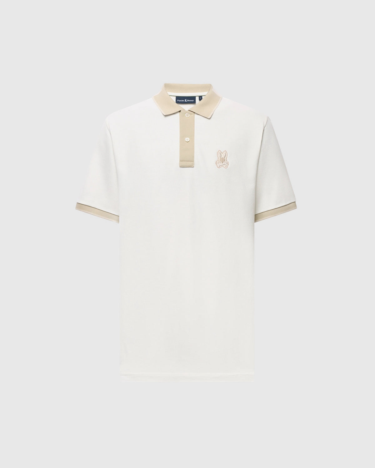 The Psycho Bunny MENS NEW CASTLE PIQUE POLO (B6K487F200) is a slim-fit, short-sleeve off-white polo with beige contrast on the collar, cuffs, and placket, plus an embroidered bunny logo on the chest. Displayed on a light gray background.