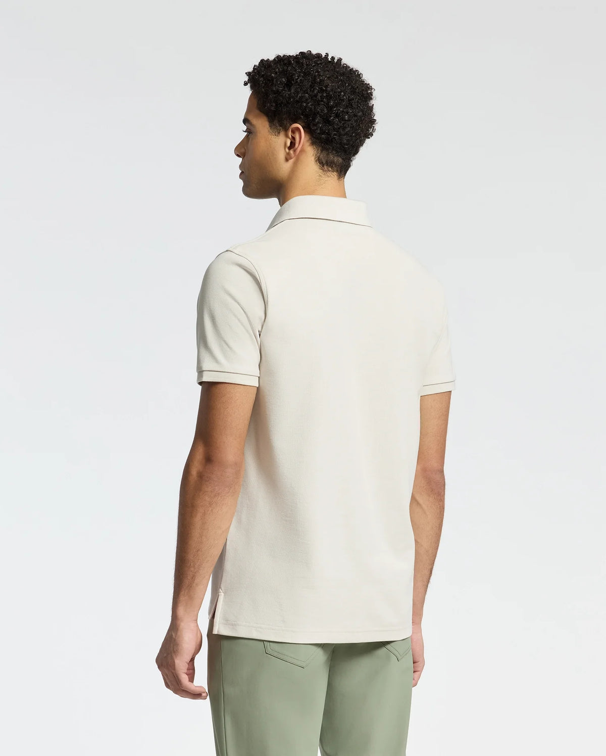 A man wearing a Psycho Bunny MENS DESERT PIQUE POLO - B6K506F200, made of Pima cotton in a classic design, stands with his back to the camera against a plain white background.