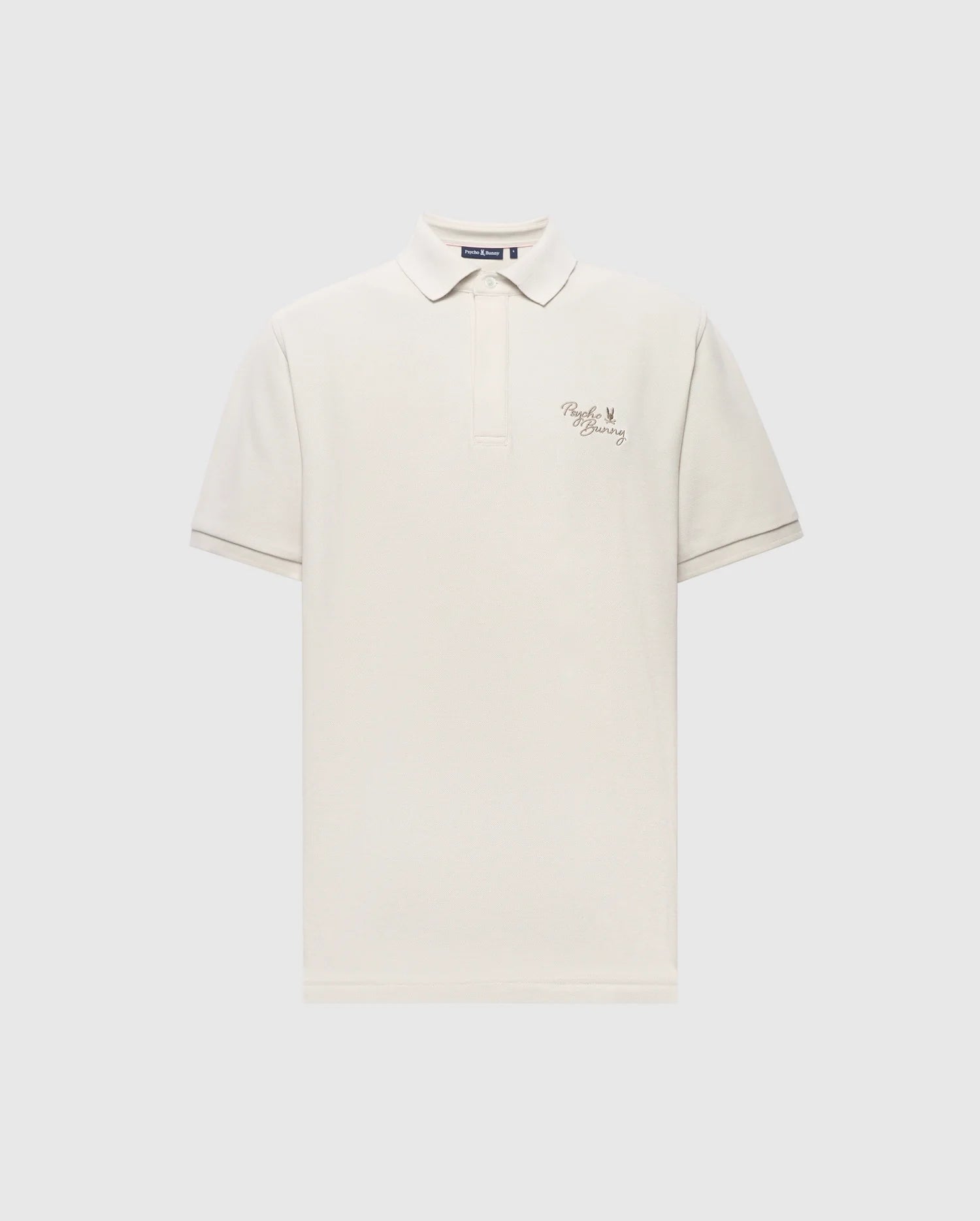 The Psycho Bunny MENS DESERT PIQUE POLO - B6K506F200 is crafted from soft Pima cotton, featuring a white color with a collar and buttoned placket. It showcases text and a small heart design on the left chest against a light gray background, offering timeless style.