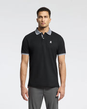 A man wears a Psycho Bunny MENS JONAS STRIPE COLLAR PIQUE POLO - B6K583F200. It's black, made from luxurious Pima Cotton with a gray collar and sleeve trim, featuring a small white emblem on the chest, showcasing its premium Peruvian quality against a plain white backdrop.