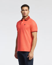 A man with short hair wears the Psycho Bunny "MENS JONAS MICRO STRIPE COLLAR PIQUE POLO - B6K583F200," an orange Pima Cotton shirt with a micro-stripe design, dark brown collar, sleeve trim, regular fit, and a small bird logo on the chest. He stands against a plain background, looking directly at the camera.