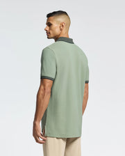 A man faces away wearing a mint green Psycho Bunny Jonas Micro Stripe Collar Pique Polo, crafted from Pima cotton with dark trim, paired with beige pants against a plain light background.