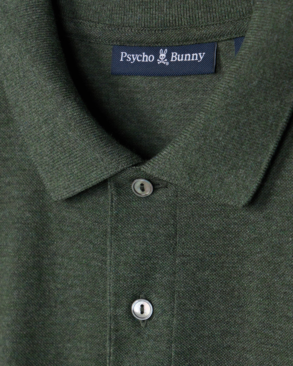 Close-up of a green Psycho Bunny MENS JAMES PREMIUM PIQUE POLO SHIRT - B6K945D200, showcasing its lightweight pima cotton fabric, collar, two buttons, and the brand label on the inner collar.