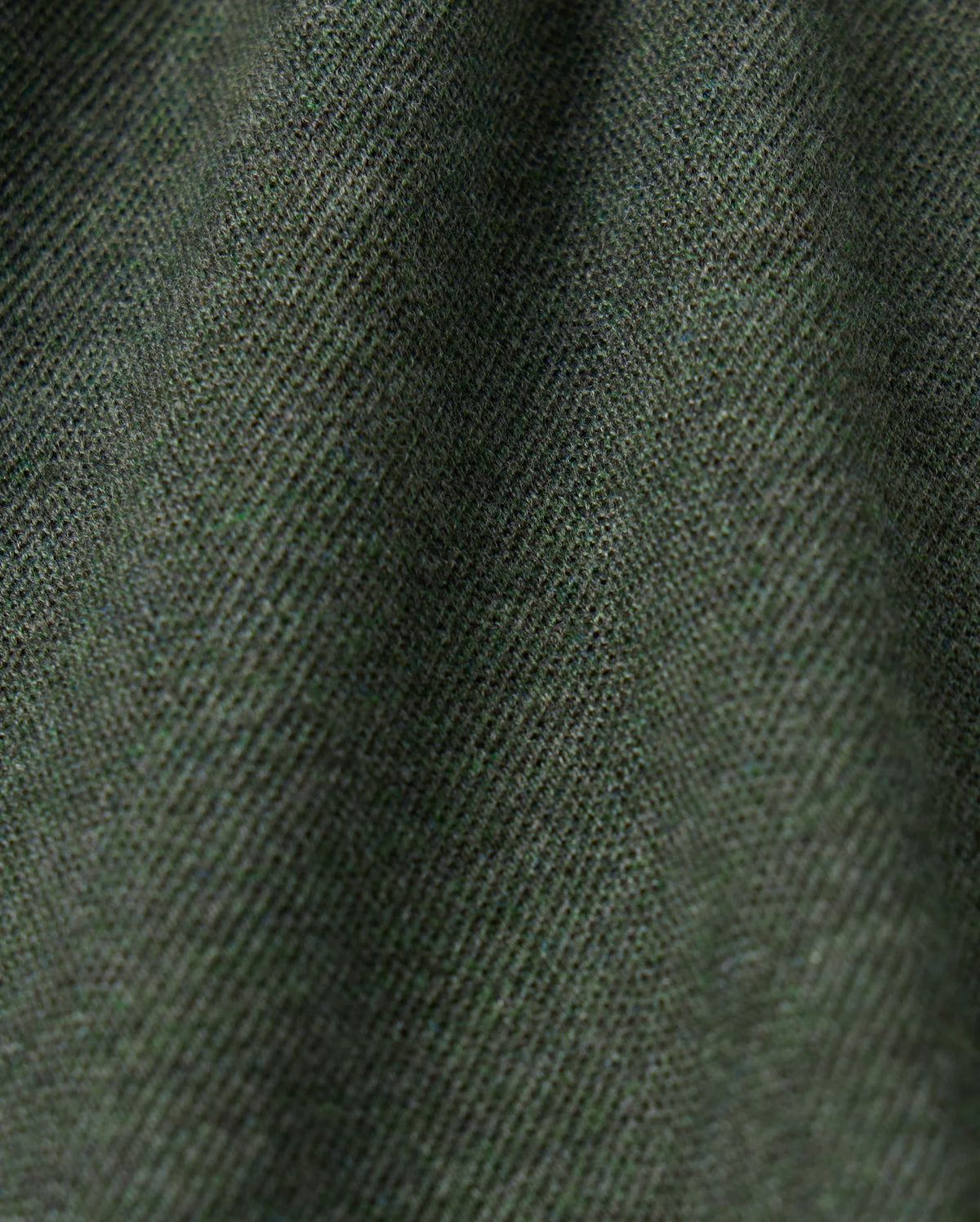 Close-up view of the textured fabric in a dark green color. The high-quality MENS JAMES PREMIUM PIQUE POLO SHIRT by Psycho Bunny features a soft, slightly fuzzy surface with fine threads woven tightly together, creating a subtle diagonal pattern. The lightweight pima cotton material appears slightly draped, showing gentle folds.