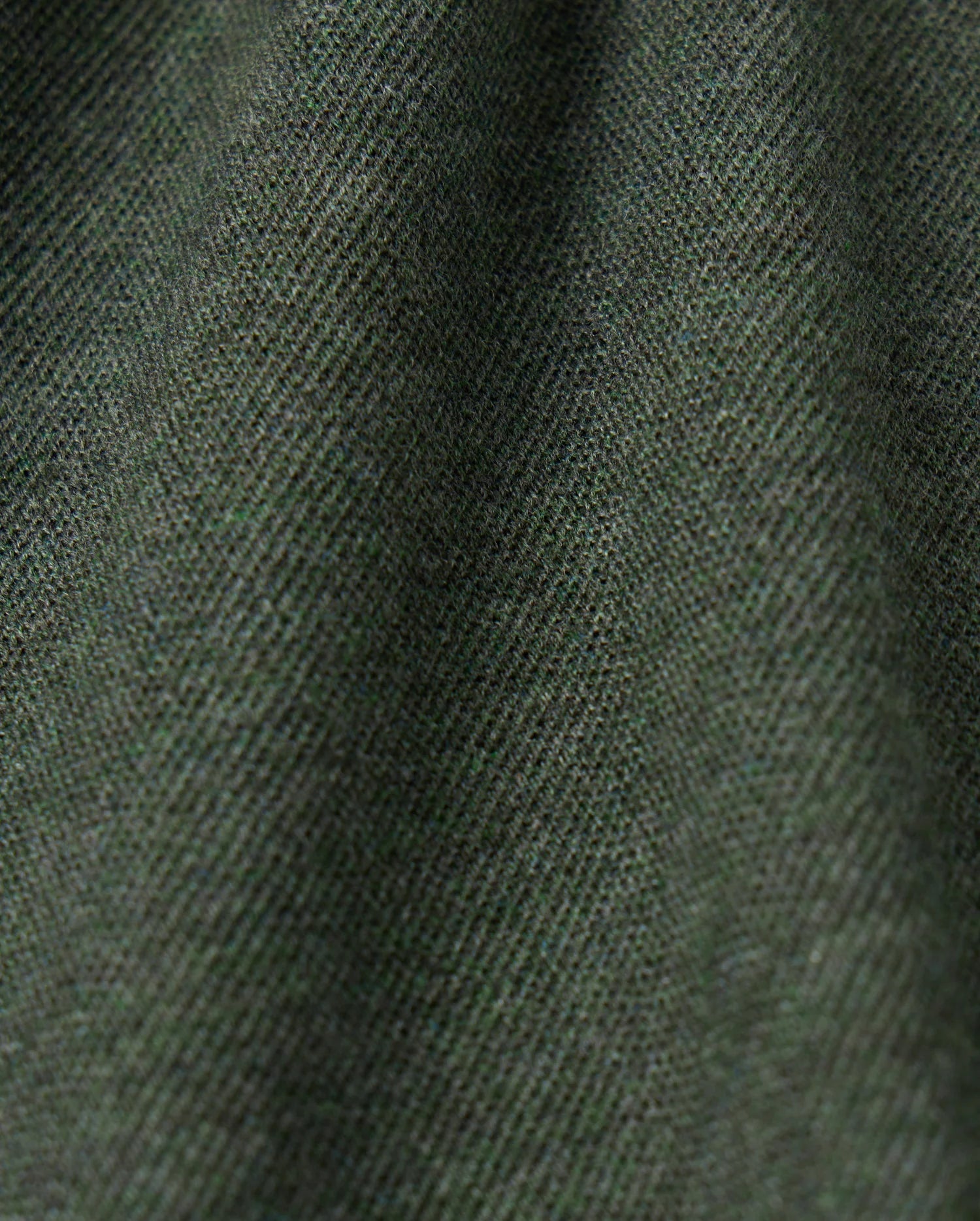 Close-up view of the textured fabric in a dark green color. The high-quality MENS JAMES PREMIUM PIQUE POLO SHIRT by Psycho Bunny features a soft, slightly fuzzy surface with fine threads woven tightly together, creating a subtle diagonal pattern. The lightweight pima cotton material appears slightly draped, showing gentle folds.