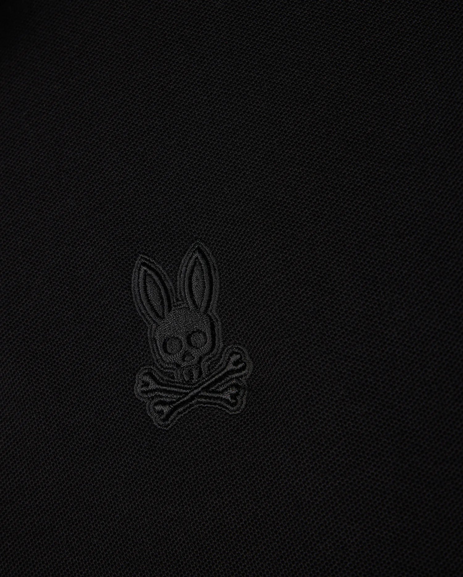 A black fabric featuring a stitched design of Psycho Bunny’s iconic skull with bunny ears and crossbones, all in a slightly different shade of black for subtle contrast – reminiscent of the stylish MENS MALTON PIQUE POLO SHIRT by Psycho Bunny (B6K950D200).