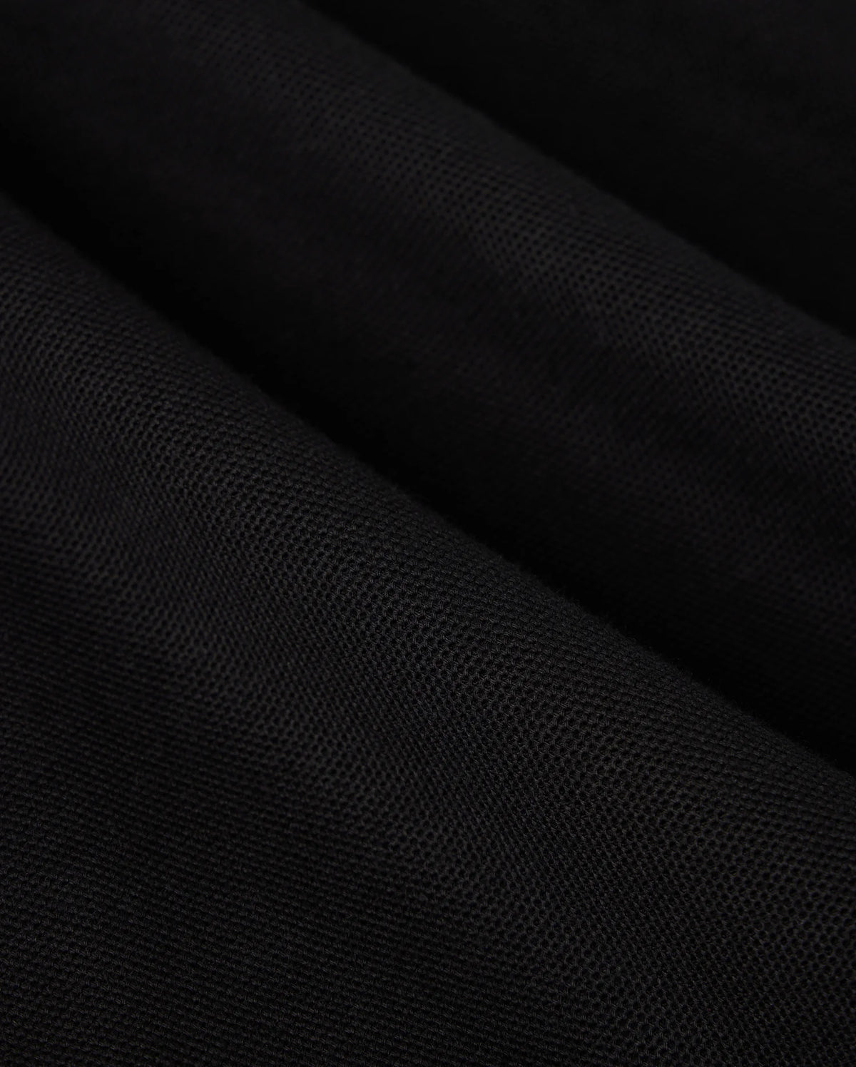 Close-up view of a black Pima cotton MENS MALTON PIQUE POLO SHIRT - B6K950D200, showcasing its texture and weave pattern. The material is slightly folded, creating diagonal lines and subtle highlights. The Psycho Bunny surface appears smooth and uniform, accentuating the exquisite detail.