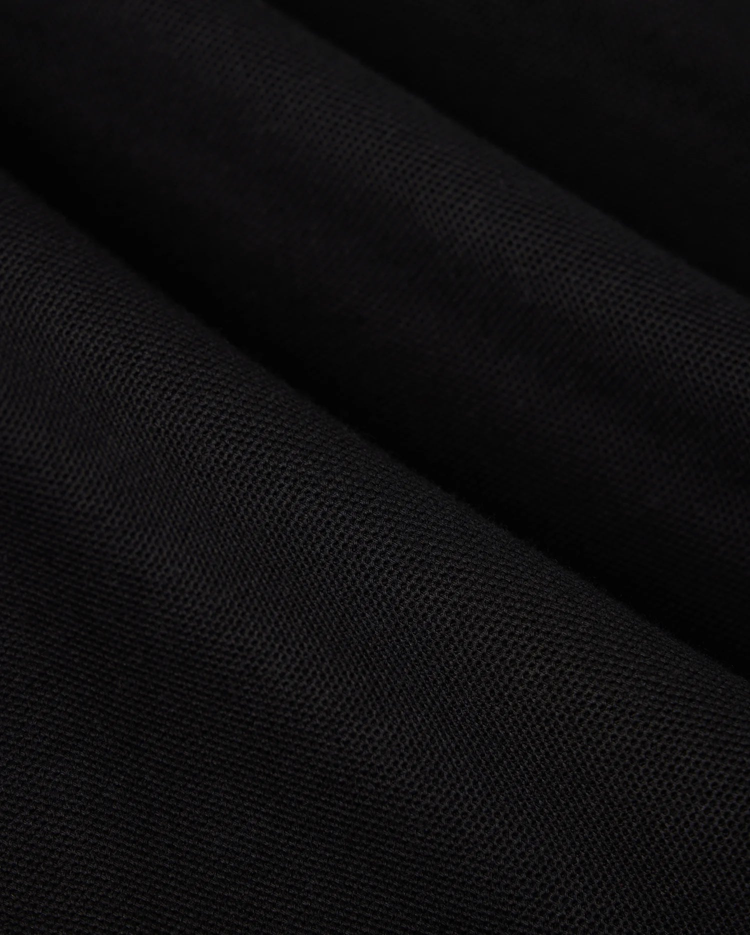 Close-up view of a black Pima cotton MENS MALTON PIQUE POLO SHIRT - B6K950D200, showcasing its texture and weave pattern. The material is slightly folded, creating diagonal lines and subtle highlights. The Psycho Bunny surface appears smooth and uniform, accentuating the exquisite detail.