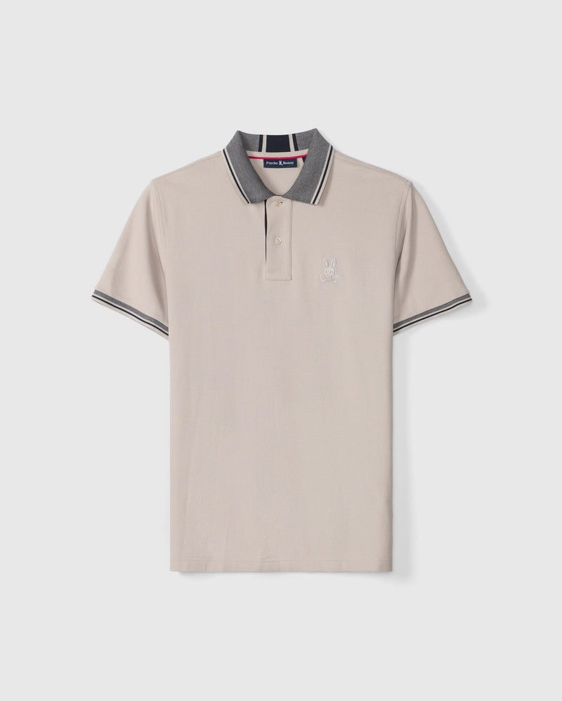 The Psycho Bunny Men's Malton Pique Polo Shirt (B6K950D200) is made from light beige Pima cotton and features a stylish gray collar and sleeve cuffs. It includes a sleek, buttoned placket, sporty trim details, and an embroidered Psycho Bunny logo on the left chest.