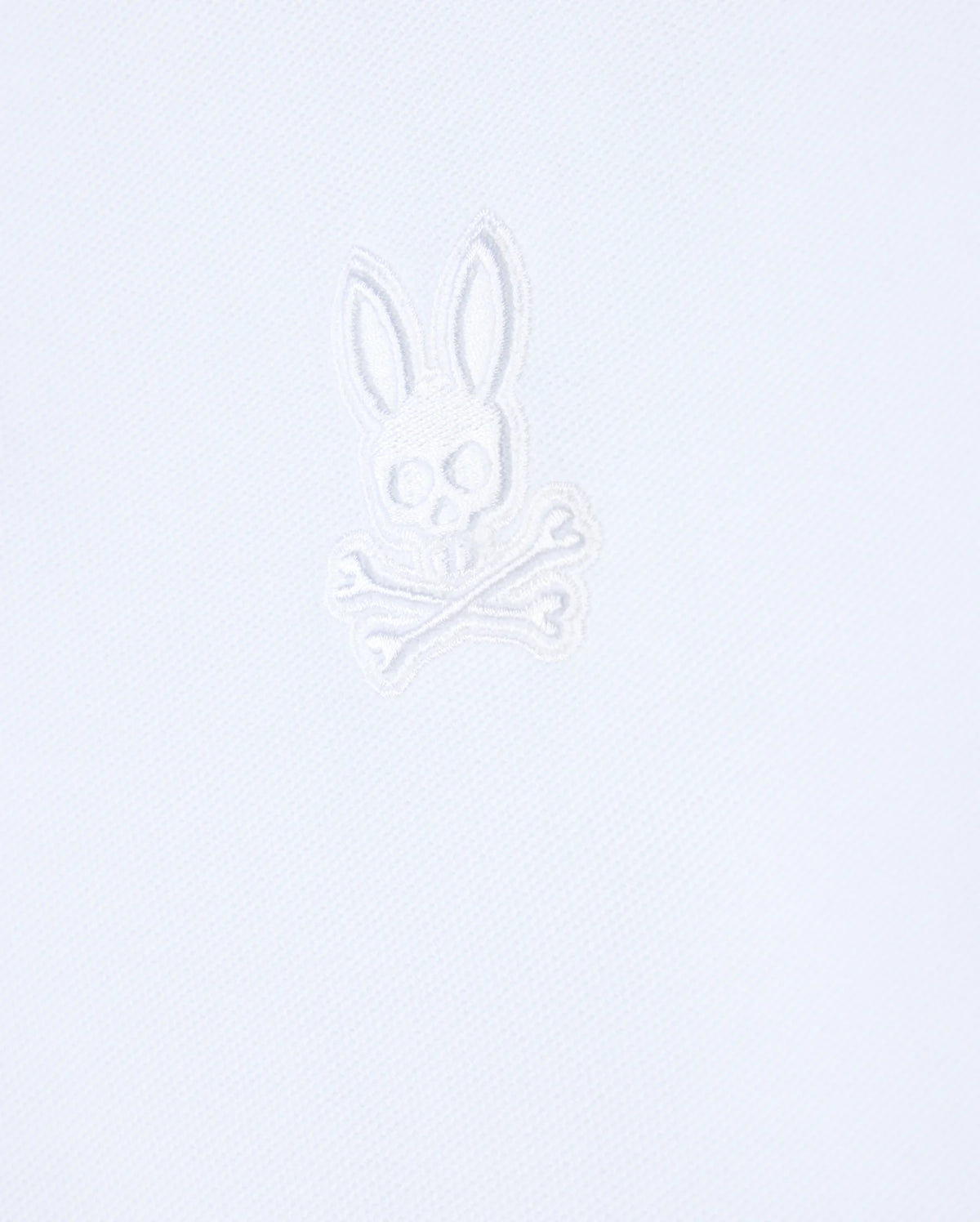 Introducing the Psycho Bunny Mens Malton Pique Polo Shirt - B6K950D200, crafted from a white textured fabric that features an embroidered stylized skull with rabbit ears above crossed bones in white thread, embodying the iconic Psycho Bunny aesthetic.
