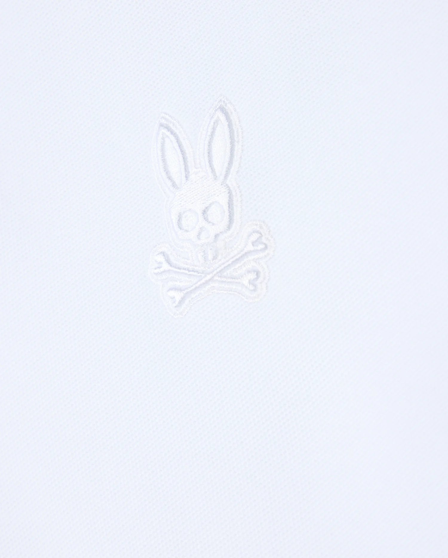 Introducing the Psycho Bunny Mens Malton Pique Polo Shirt - B6K950D200, crafted from a white textured fabric that features an embroidered stylized skull with rabbit ears above crossed bones in white thread, embodying the iconic Psycho Bunny aesthetic.