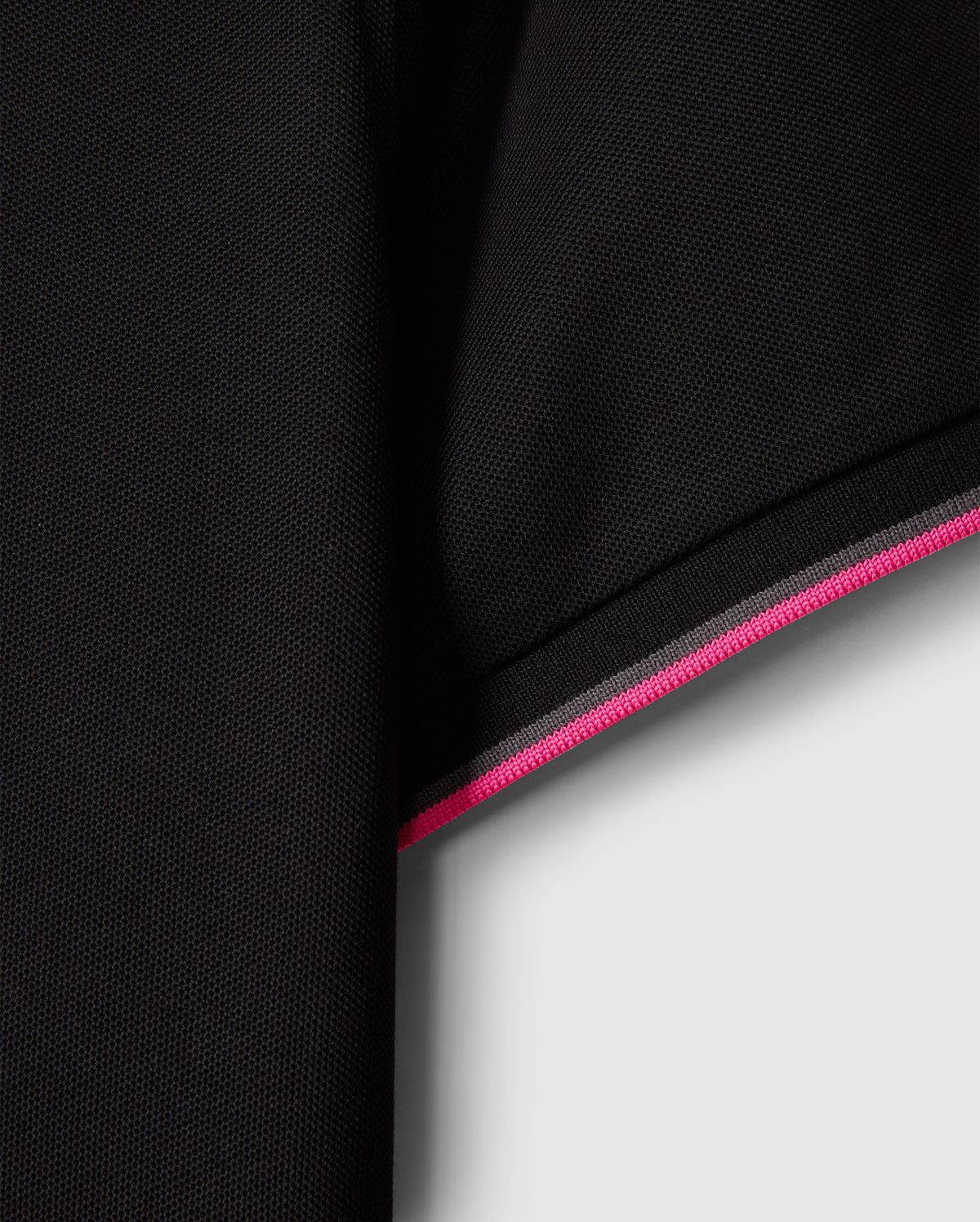 Close-up of a black fabric sleeve from the MENS KENT PIQUE POLO SHIRT - B6K951D200 by Psycho Bunny, featuring an edge with pink and white stripes that evoke the style of a fashionable polo. The material is subtly textured, displaying a delicate woven pattern. The contrast between the dark fabric and the vivid stripes enhances this comfortable piece's stylish appeal.