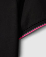 Close-up of a black fabric sleeve from the MENS KENT PIQUE POLO SHIRT - B6K951D200 by Psycho Bunny, featuring an edge with pink and white stripes that evoke the style of a fashionable polo. The material is subtly textured, displaying a delicate woven pattern. The contrast between the dark fabric and the vivid stripes enhances this comfortable piece's stylish appeal.