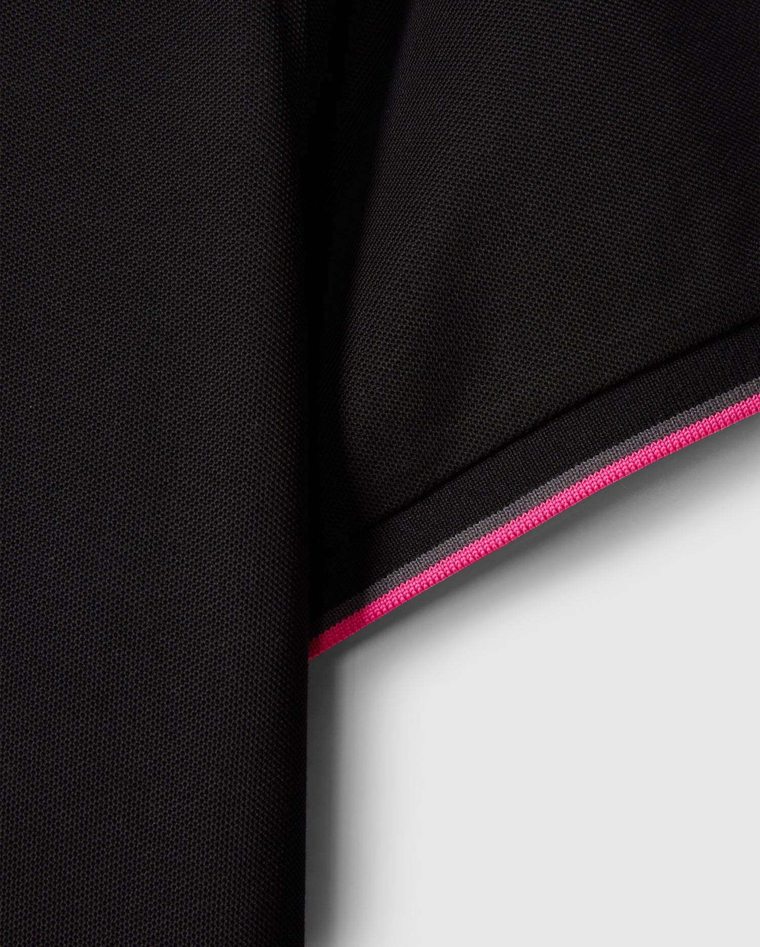 Close-up of a black fabric sleeve from the MENS KENT PIQUE POLO SHIRT - B6K951D200 by Psycho Bunny, featuring an edge with pink and white stripes that evoke the style of a fashionable polo. The material is subtly textured, displaying a delicate woven pattern. The contrast between the dark fabric and the vivid stripes enhances this comfortable piece's stylish appeal.