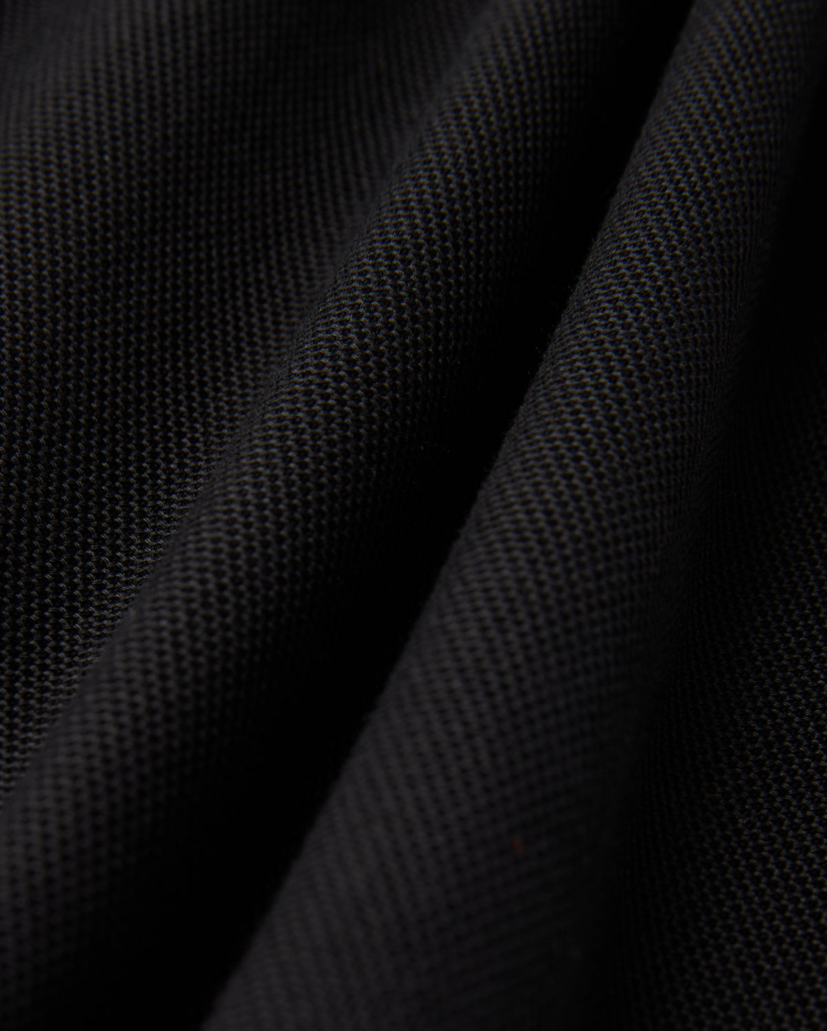 Close-up of a black textured fabric, evocative of the Psycho Bunny MENS KENT PIQUE POLO SHIRT - B6K951D200, showcasing a subtle woven pattern and gentle folds, which impart a sense of depth and softness.