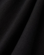 Close-up of a black textured fabric, evocative of the Psycho Bunny MENS KENT PIQUE POLO SHIRT - B6K951D200, showcasing a subtle woven pattern and gentle folds, which impart a sense of depth and softness.