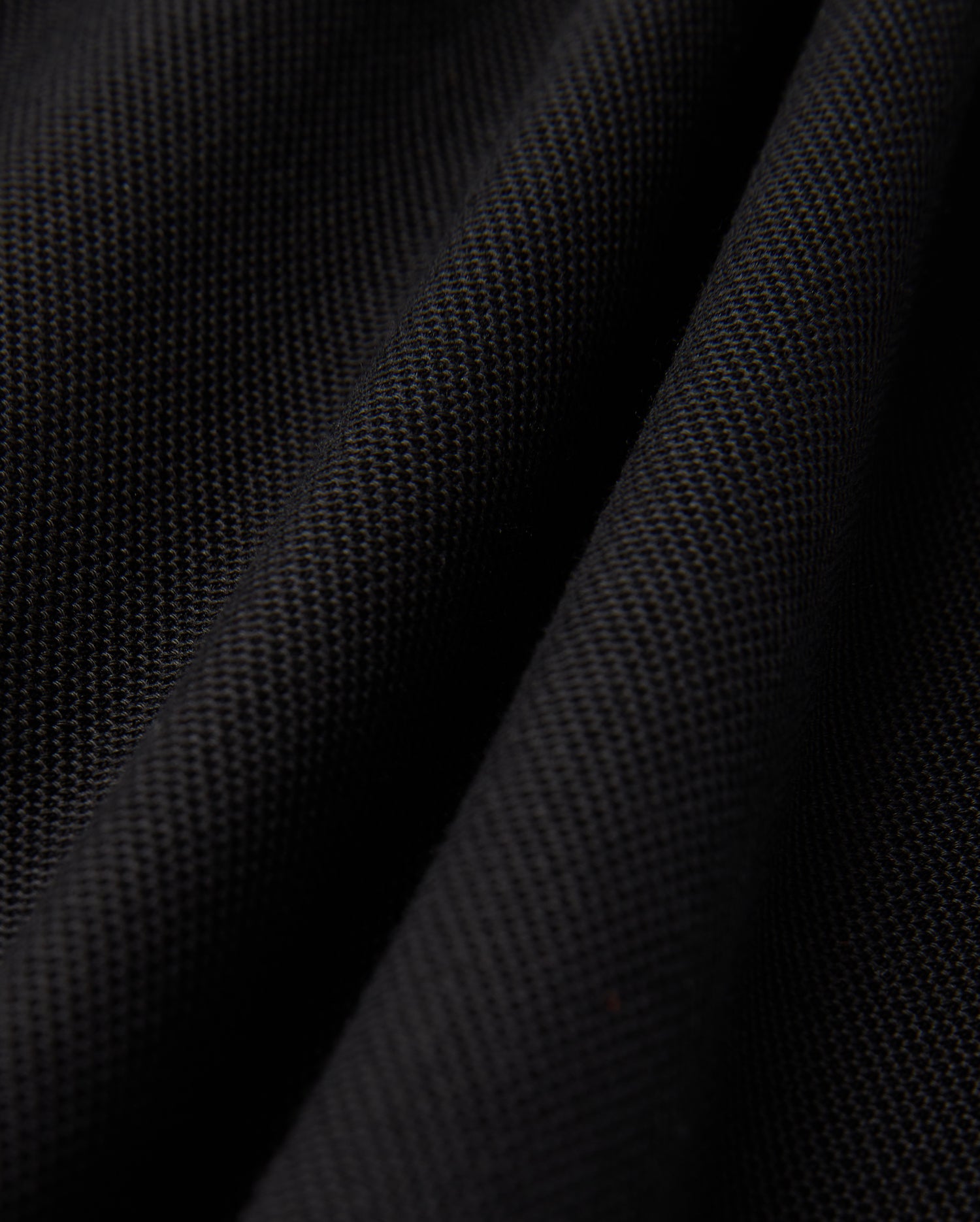 Close-up of a black textured fabric, evocative of the Psycho Bunny MENS KENT PIQUE POLO SHIRT - B6K951D200, showcasing a subtle woven pattern and gentle folds, which impart a sense of depth and softness.