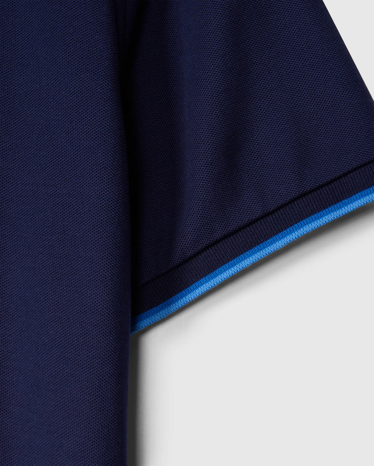 Close-up of the Psycho Bunny MENS KENT PIQUE POLO SHIRT - B6K951D200, showcasing the dark blue fabric sleeve with a light blue trim. The Pima cotton texture is visible against a light background.