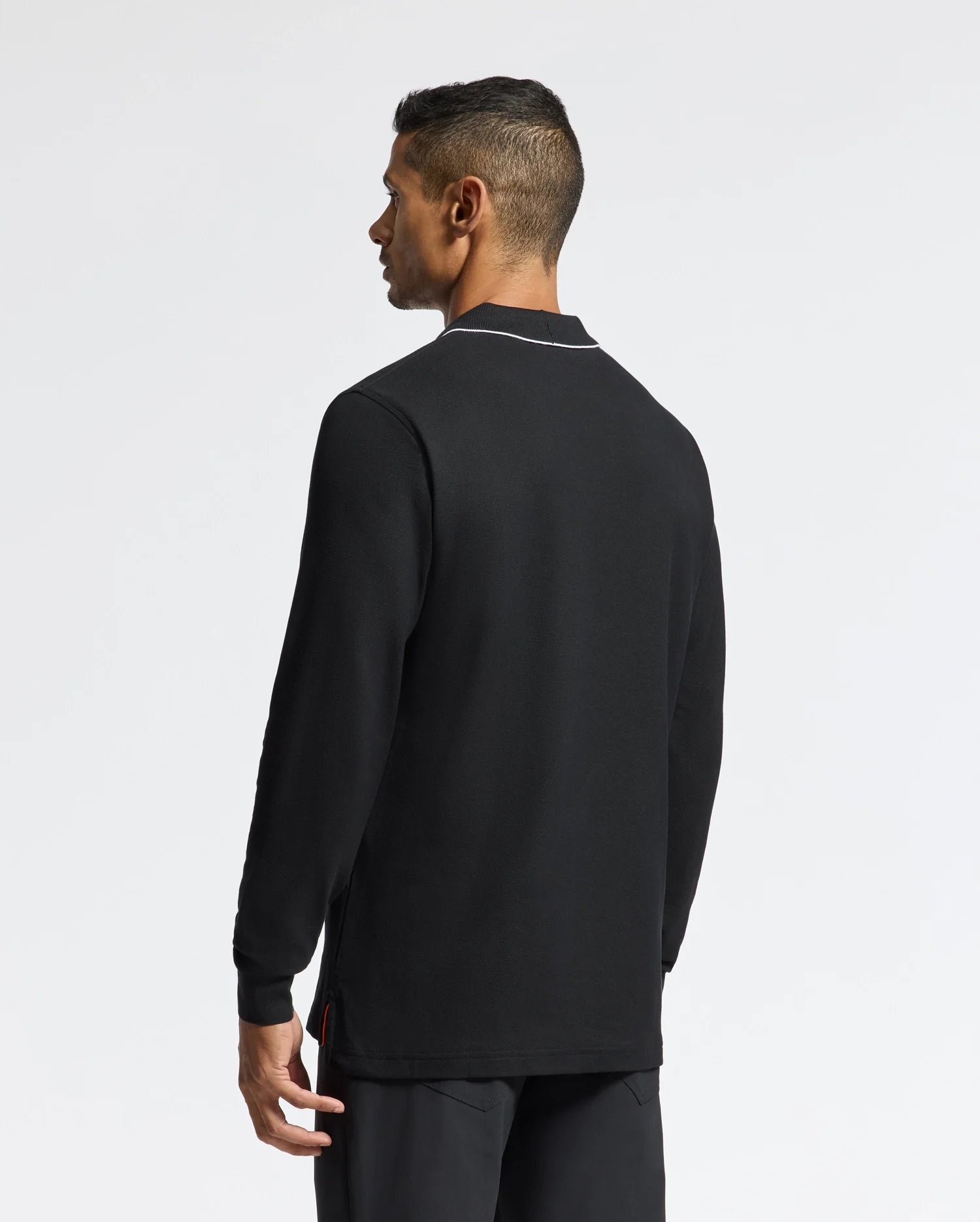 A person with short dark hair is standing and facing away from the camera, wearing a Psycho Bunny MENS CREEDE PIQUE JOHNNY COLLAR POLO (B6M265E200) made of Pima Cotton and featuring a subtle white outline around the collar, paired with dark pants against a plain light background.