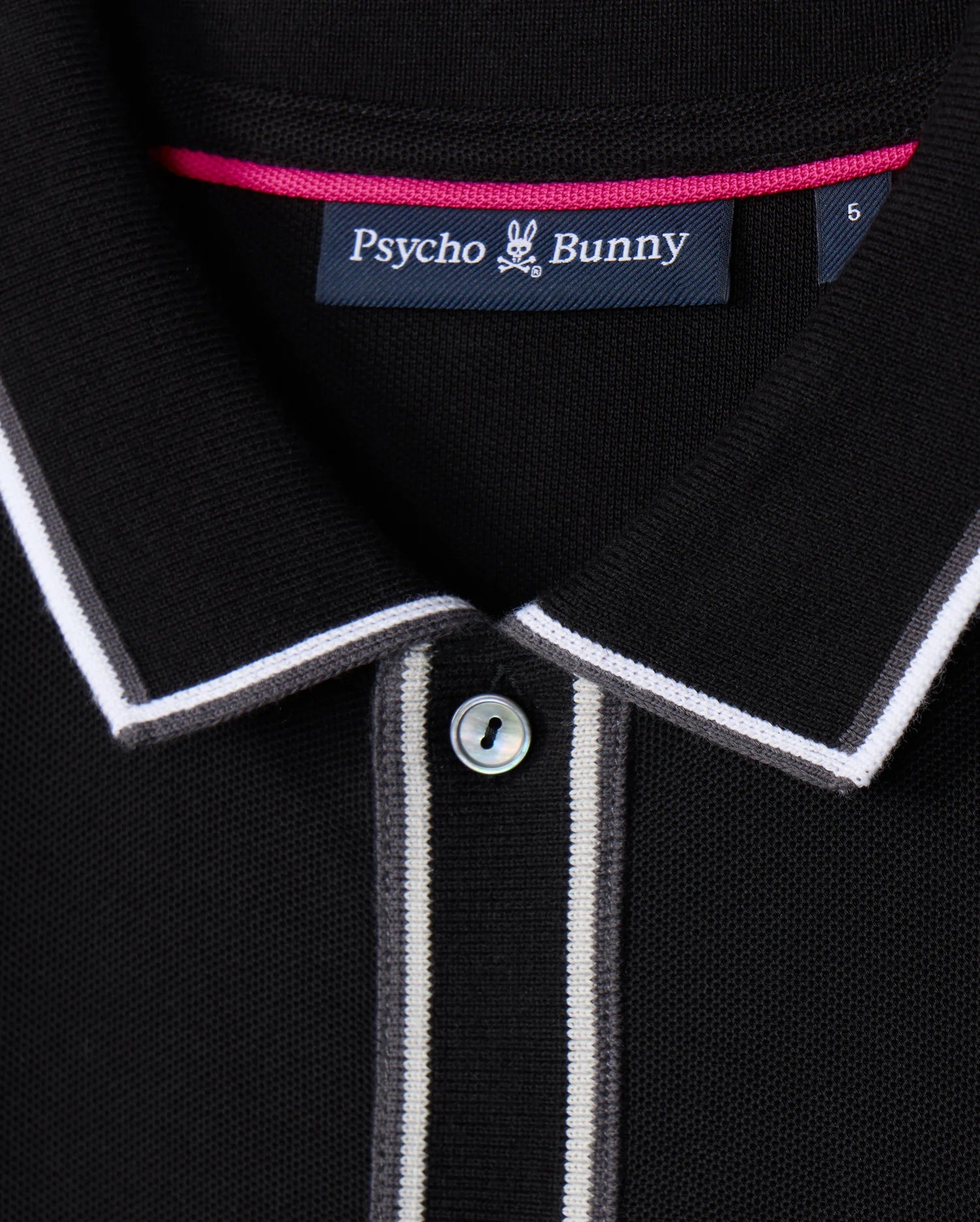A detailed view of the Psycho Bunny Men's Kent Long Sleeve Pique Polo in black showcases its sophisticated design, featuring a button and white and gray striped accents on the collar and placket. Made from high-quality Pima cotton, it includes a "Psycho Bunny" label inside the collar.