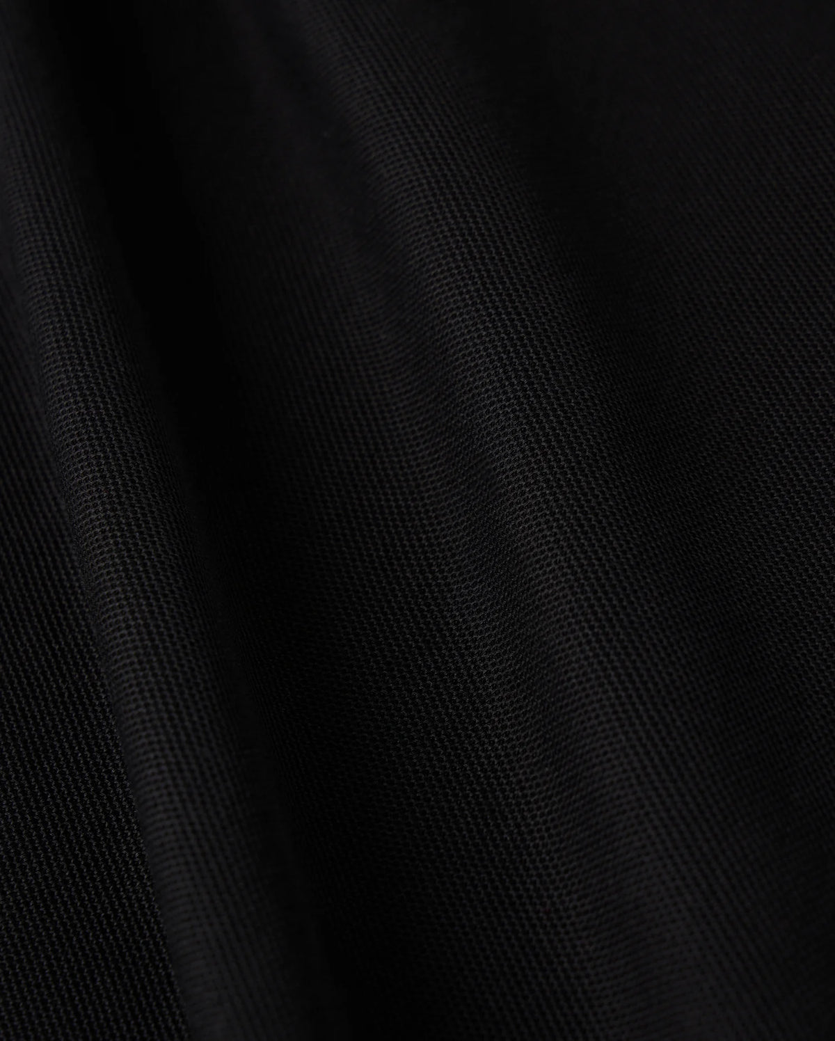 Close-up of the black Pima cotton fabric from the Psycho Bunny MENS KENT LONG SLEEVE PIQUE POLO - B6M935D200, featuring a soft texture and subtle diagonal lines that enhance its depth and smoothness. The material offers a velvety touch with a slight sheen under light, embodying quiet luxury with its rich, dark tone.