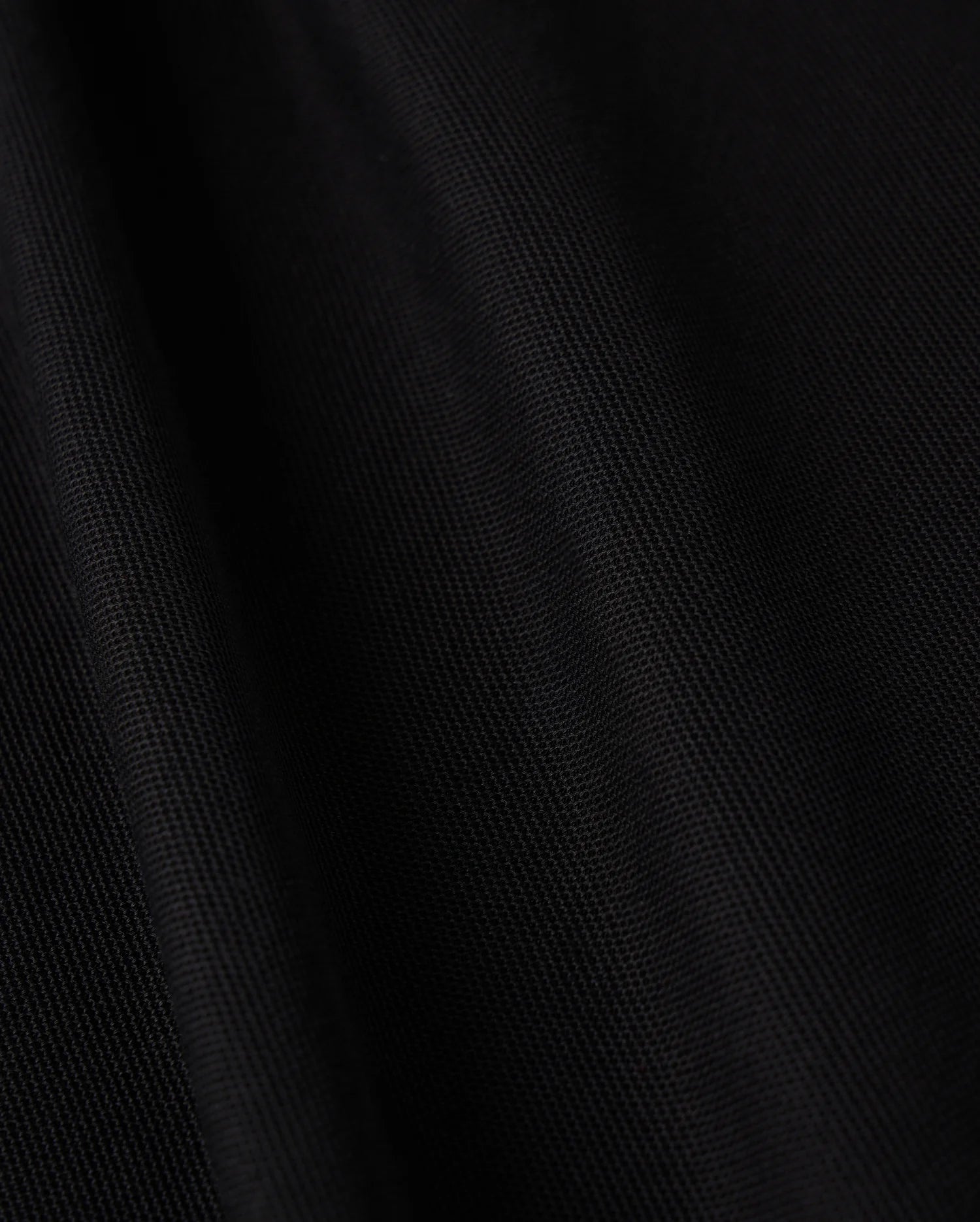 Close-up of the black Pima cotton fabric from the Psycho Bunny MENS KENT LONG SLEEVE PIQUE POLO - B6M935D200, featuring a soft texture and subtle diagonal lines that enhance its depth and smoothness. The material offers a velvety touch with a slight sheen under light, embodying quiet luxury with its rich, dark tone.