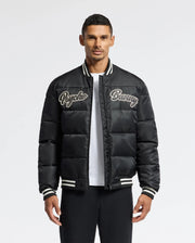 A man in a black MENS FRASER FASHION PUFFER - B6N338E200 by Psycho Bunny stands against a plain background. The lightweight jacket features white striped cuffs and collar, which he pairs stylishly with a white T-shirt underneath and black pants.