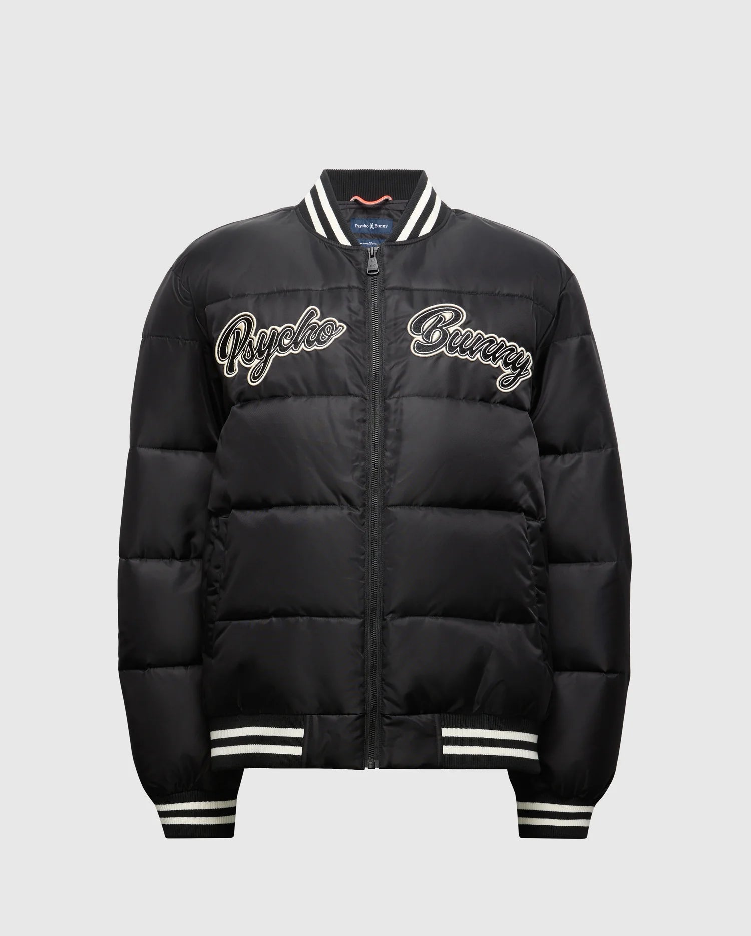 Introducing the MENS FRASER FASHION PUFFER - B6N338E200 by Psycho Bunny: a black puffer jacket adorned with white embroidered "Psycho Bunny" text on the front. This lightweight men's coat features a striped collar, cuffs, and hem, along with a convenient front zip closure. Its casual and sporty design makes it an ideal choice for any men's fashion enthusiast.