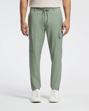 A person models the Psycho Bunny MENS LLOYD CARGO JOGGER - B6P159B200 in sage green, featuring stretch twill, side pockets, and a drawstring waist. Paired with a white shirt and sleek sneakers, the plain background enhances the ensemble's embroidered refinement.