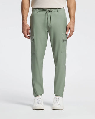 A person models the Psycho Bunny MENS LLOYD CARGO JOGGER - B6P159B200 in sage green, featuring stretch twill, side pockets, and a drawstring waist. Paired with a white shirt and sleek sneakers, the plain background enhances the ensemble's embroidered refinement.